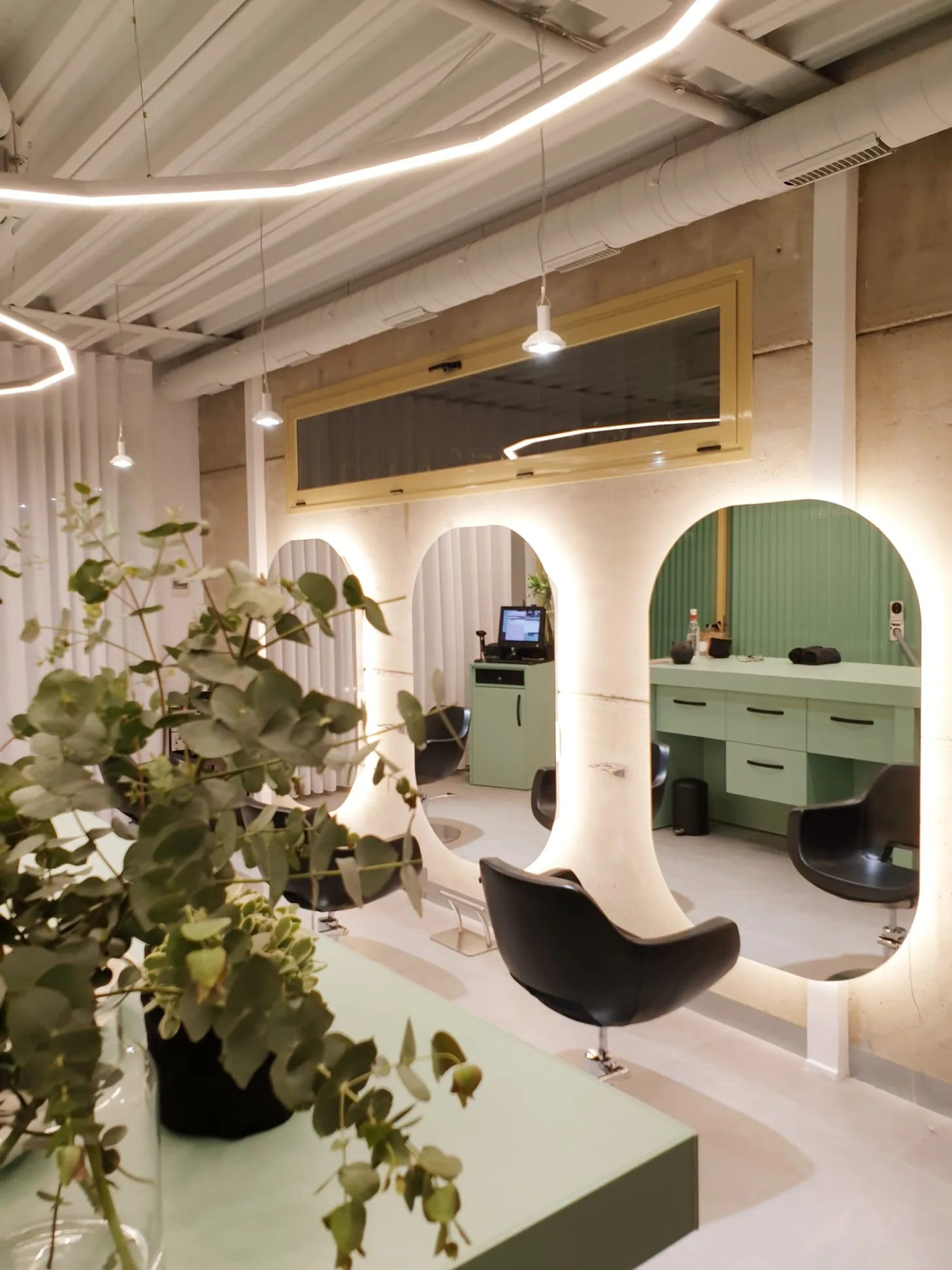 Sala principal de LOAL: tres puestos de peluquería recortados en arcos de luz sobre pilares de hormigón visto, con tocadores verde salvia.